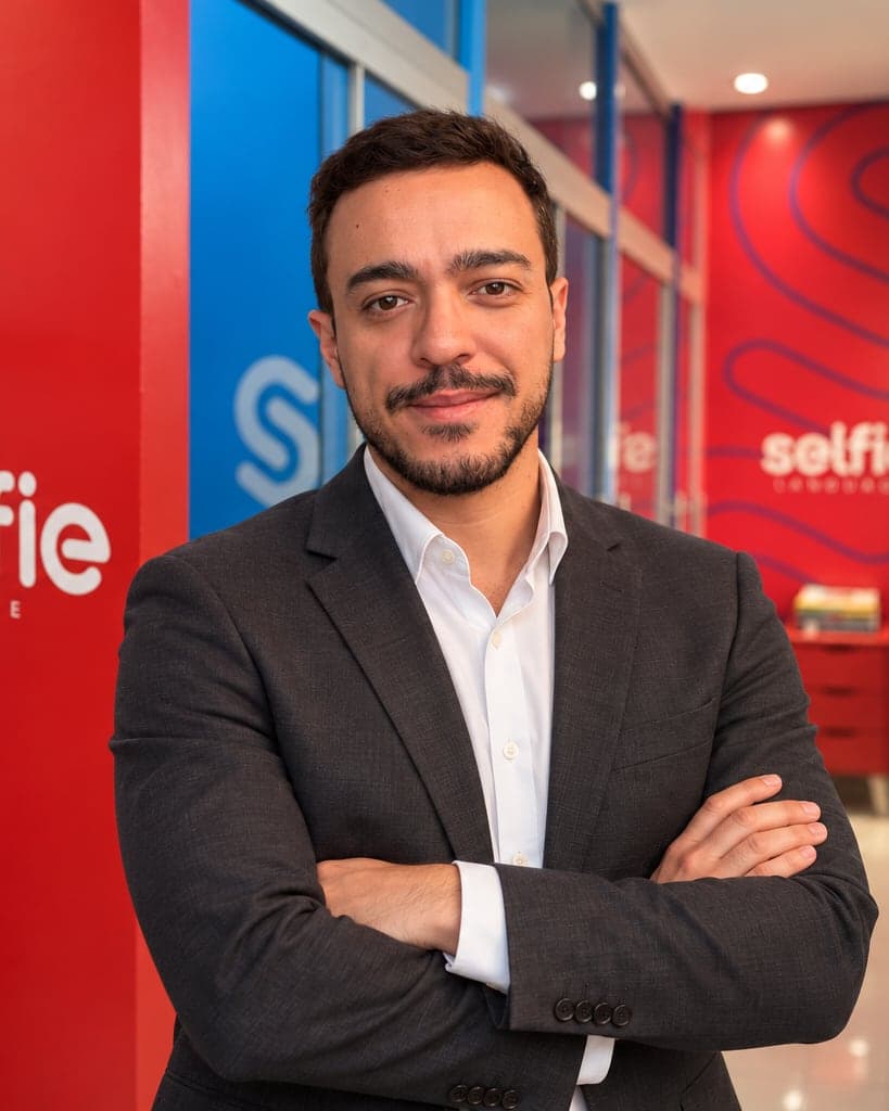 De blazer, no corredor da Selfie, com a parede da marca ao fundo.